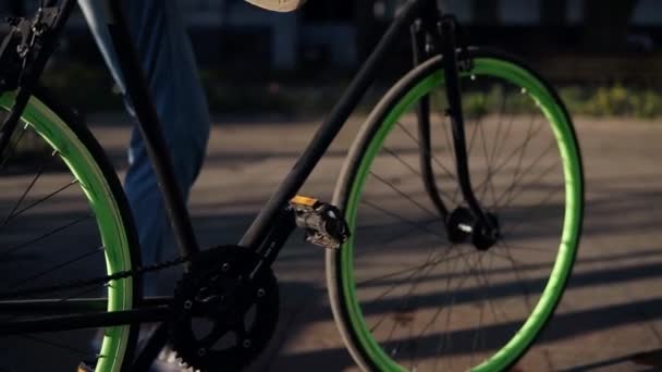 Close-up beelden van een jong meisje in jeans en sneakers beginnen met haar trekking fiets met groene wielen, pedalen te duwen. Stadszijde, lens flares. Zeldzame weergave — Stockvideo