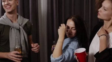 Arkadaş grubu eğleniyor. Neşeli genç insanlar dans ve oturma odasında ev partisi tadını çıkarırken içme görüntüleri