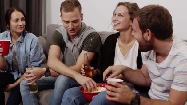Дружба, общение, веселье - веселые кавказские друзья разговаривают, веселятся, сидят на диване в помещении и смеются, едят попкорн, пьют. Мужская и женская компания. Медленное движение — стоковое видео