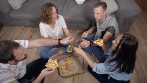 Amitié, nourriture, temps de fête domestique - des amis caucasiens joyeux commandent une pizza, s'amusent, s'assoient sur le sol en bois à l'intérieur et rient, mangent, boivent, applaudissent. Vue du dessus — Video