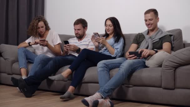 Diversos jóvenes sentados en fila en el sofá juntos obsesionados con los dispositivos en línea, adictos caucásicos utilizando sus teléfonos inteligentes, la vida digital y el concepto de abuso de gadgets. Vista de ángulo bajo — Vídeos de Stock