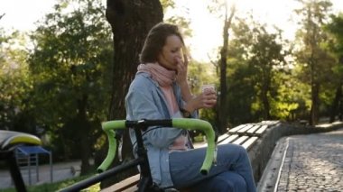 Bisiklet yanında olan parkta bir bankta dinlendirici bir gün kahve içme beyaz genç kız. Sabah güneş ışığı üzerinde arka plan olduğunu.