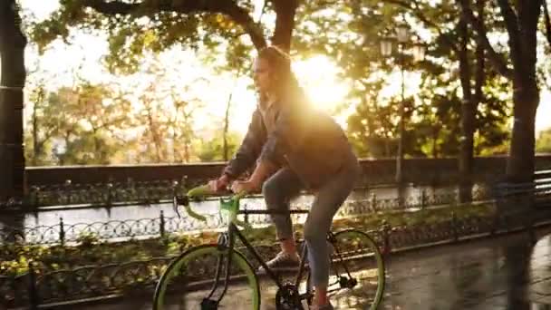 Bella femmina caucasica in bicicletta nel parco o nel viale del mattino. Vista laterale di una giovane donna che guida una trekking bike, indossa scarpe da ginnastica e vestiti casual — Video Stock