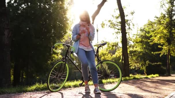 可爱的女孩喝清澈的水从瓶子户外, 靠在她徒步旅行绿色车轮自行车。美丽的自然背景, 镜头耀斑 — 图库视频影像