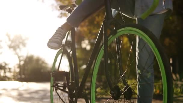 Close up filmagem de uma jovem em jeans e tênis começando a andar de bicicleta de trekking com rodas verdes, empurrando pedais. Lado da cidade, lentes acesas, sem rosto. Vista frontal — Vídeo de Stock