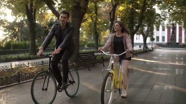 Casal jovem caucasiano ou amigos andando de bicicleta no vazio parque da cidade ou avenida no verão. Pessoas, lazer e conceito de estilo de vida. Sinalizadores de lente — Vídeo de Stock