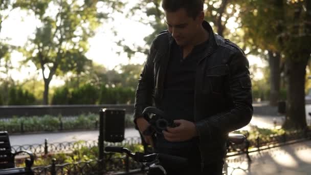 Estilo de vida, transporte, tecnologia e conceito de pessoas - o jovem com fones de ouvido começa a andar de bicicleta na rua da cidade, escolhendo os mucis favoritos em seu smartphone. Outono no parque da cidade — Vídeo de Stock