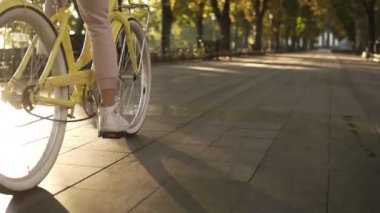 Kadın meçhul bacaklar bisikletle döşeli yolda yürürken yan görünümü aktif yaşam tarzı kapatın. Kadın kız vintage Kiralama ile cadde ve yeşil park ediyor. Sağlıklı yaşam, arka plan üzerinde güneş parlıyor