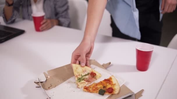 Junge leger gekleidete Mitarbeiter, die sich nach getaner Arbeit neu erschaffen.müde Mitarbeiter, die im modernen Interieur-Büro Pizza essen — Stockvideo