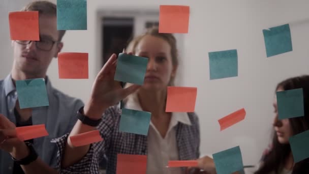 Diverse team of young people young business people while working together during brainstorming and standing behind glass wall with sticky colorful papers — Stock Video