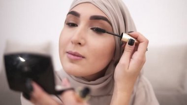 Çekici Müslüman kadın profesyonel makyaj yapıyor. Kirpik maskara ile fırça. Bej başörtüsü takıyor. Arka plan üzerinde beyaz duvar