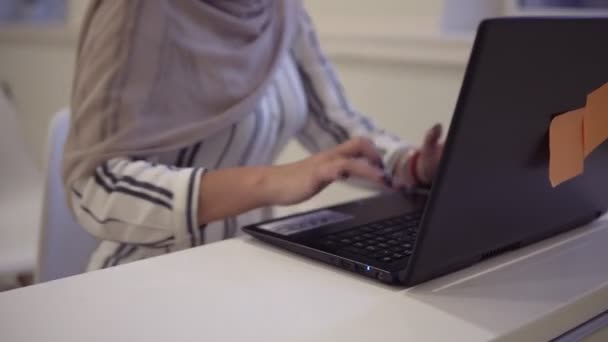 Χαμογελώντας αυτοπεποίθηση μουσουλμανική γυναίκα φορούσε ένα hijab που κάθεται στις λευκές καρέκλες στην αίθουσα συνεδρίων του σύγχρονου online με ένα laptop στο λευκό γραφείο, δακτυλογράφηση, ασύρματο εργασίας — Αρχείο Βίντεο