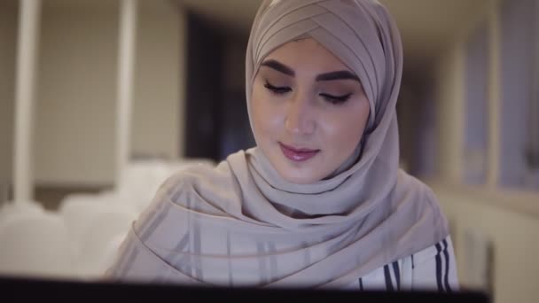 特写视图穆斯林女性脸穿着米色盖头坐在现代会议厅在线与笔记本电脑。前视图 — 图库视频影像
