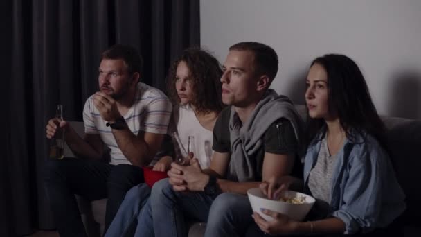 Los mejores amigos que comen palomitas de maíz, beben cerveza ven películas de terror juntos y están muy cautivados y asustados, se quedan quietos. Cierra los ojos de la imagen aterradora. Noche de cine — Vídeo de stock