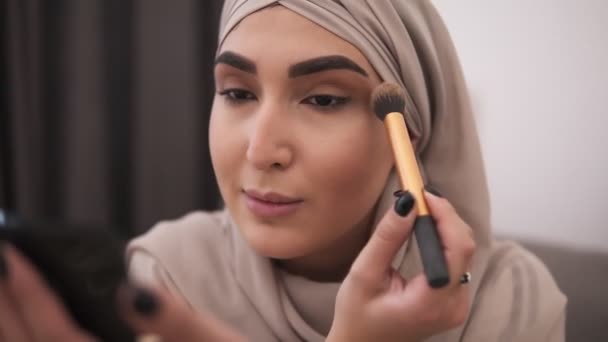 Närbild av muslimsk kvinna gör makeup på hennes ansikte med borste, ansöker ögonskuggor. Moderna livet av muslimska människor, smink hemma, ofokuserad bakgrunden Visa — Stockvideo