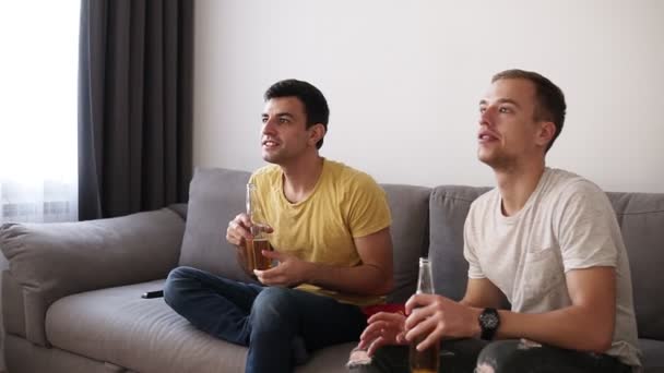 Dos amigos adultos emocionados bebiendo cerveza y viendo el partido de fútbol en el interior de la televisión con interés. Levántate del sofá, celebrando emocionalmente la victoria. De cerca. — Vídeos de Stock