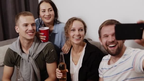 Stijlvolle, moderne en aantrekkelijke positieve vrienden zitten in woonkamer, drinkbekers en zuigflessen in handen, met selfie schieten op slimme telefoon, lachen, tonen tongen — Stockvideo