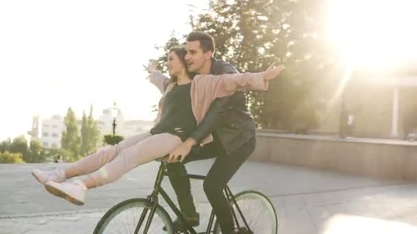 Радость и счастье молодой пары весело кататься на одном велосипеде на открытом воздухе деятельности с подсветкой на заднем плане. Человек, романтика, концепция досуга — стоковое видео