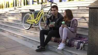 Genç ouple üstünde belgili tanımlık merdiven ve gitar çalmak adam oturan çift. Kız arkadaşıyla açık havada ekose şehir merdivenlerde oturan ise siyah casual oyun gitar adam. Bisiklet yanlarında. Yan