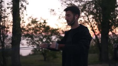 Kol işi sakallı adam açık havada direniş band kullanarak açık havada doğa çalışmaları. Sabah alacakaranlıkta, ağaçlar siluetleri arka planda. Yakın çekim