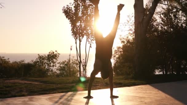 Joven haciendo la parada de manos fuera del atardecer o amanecer. Ejercicio atleta masculino de fitness. Deportes al aire libre entrenamiento estilo de vida fitness. Jóvenes deportes activos hombre entrenamiento fitness al aire libre — Vídeo de stock