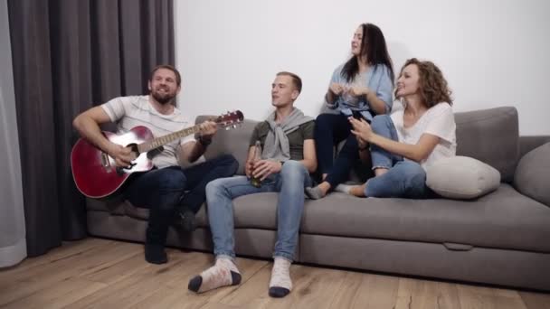 Επιταχυνόμενη πλάνα της εταιρείας τέσσερις φίλοι κάθονται στον καναπέ και να ακούσετε τύπος παίζει ακουστική κιθάρα. Πάρει μαζί για να έχουν μια καλή στιγμή με τους καλύτερους φίλους. Χορό ενώ κάθεστε, τραγουδώντας μαζί — Αρχείο Βίντεο