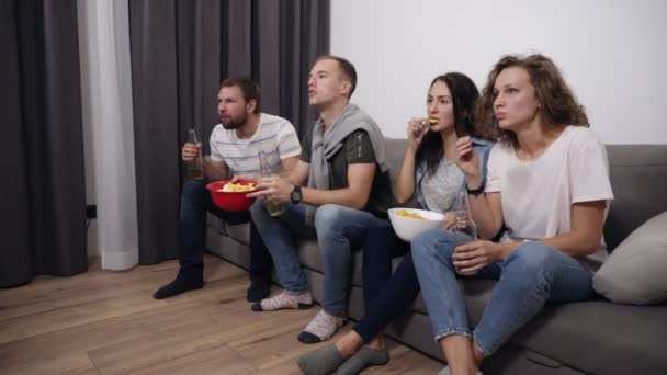 Compañía caucásica de jóvenes amigos ven el partido en la televisión con interés, experiencia y expresar sus emociones con fuerza, observando la victoria de su equipo favorito. Gritan, levantan las manos, se ponen de pie — Vídeos de Stock