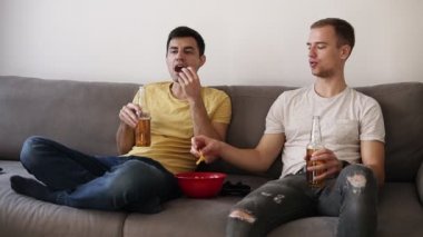 İki oda arkadaşı, kırmızı kase cips yiyip bira içmeyi rahat bir kanepe, oturma odasında oturmuş tv izlerken arkadaşlar önden görünüm