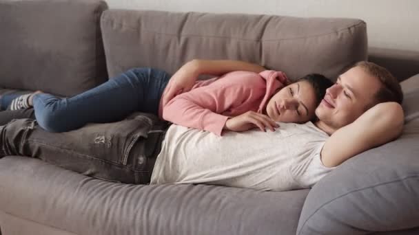Καυκάσιος ζευγάρι ξαπλωμένο στον καναπέ μαζί στο σπίτι αγκαλιάζουν. Όμορφη κοπέλα που χαϊδεύει τον φίλο του. Χαλαρώνοντας στον καναπέ — Αρχείο Βίντεο