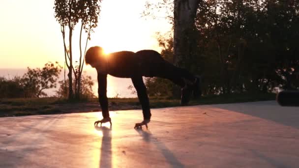 一个年轻的运动员在户外训练黑色运动服。健康的生活方式概念, 男人做俯卧撑与跳跃和交叉行动。日出清晨的背景 — 图库视频影像