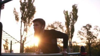 Paralel bar Park'ta sabahın kulaklık müzik dinlerken açık havada egzersiz üzerinde Triceps yapan uygun erkek dips. Güneş parlıyor ve arka plan üzerinde