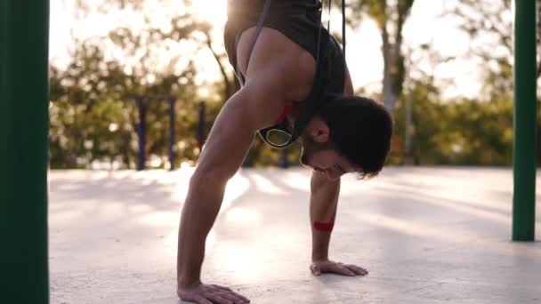 Kaukasische mannelijke atleet doet push ups terwijl staande op zijn hoofd met banden verzekering. Training op de lokale sportyard. Zonnige dag — Stockvideo