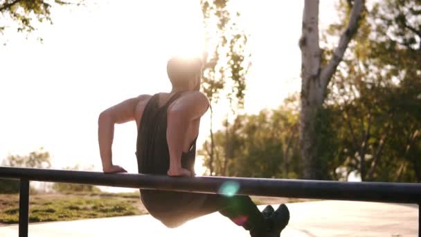 Baksidan med utsikt över en muskulös man i skjorta på lokala sport marken, träning på det horisontella tvärstaget, lutande på och göra triceps övningar på ribban. Solen skiner på bakgrunden — Stockvideo