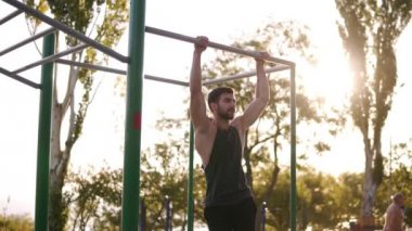 Fitness, spor, eğitim ve insan kavramı - yatay çubuk üzerinde asılı bacaklar Pull-up yapan erkek genç sakallı. Abdominal ve bacaklar açık havada spor salonunda egzersiz