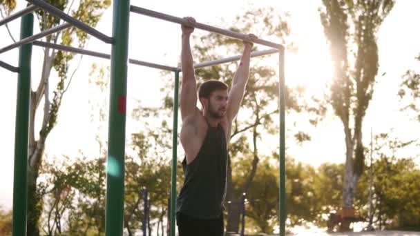 Fitness, sport, výcvik a lidé koncept - silný vousatý muž dělá cvičení nohy při zavěšení na hrazdu v parku. Břicha a nohou cvičení v tělocvičně venku. Zpomalený pohyb — Stock video