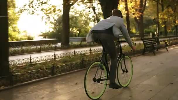 Vista rara de un joven en bicicleta en el parque y escucha la música con auriculares negros. Hombre montando su bicicleta en la mañana. Disfrutar, pasar el rato en el parque — Vídeos de Stock