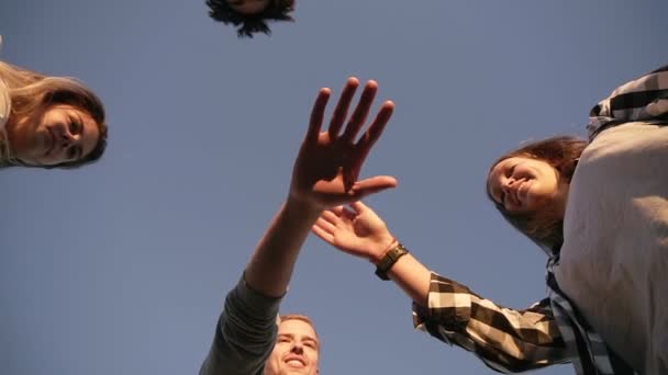 Cuatro jóvenes amigos mirando al suelo posando en un día soleado, poniendo la mano en la mano. Trabajo en equipo. Joven con estilo, feliz amistad pasando el rato juntos y sonriendo. Amistad, concepto de equipo — Vídeo de stock