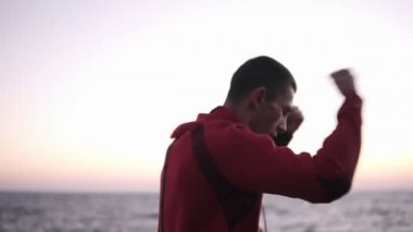 Açık havada denize yakın kadar ısınma silah, germe Genç beyaz erkek boxer. Spor, boks konsepti. Erkek atlet açık havada egzersiz kırmızı hoodie