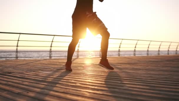 Boxer stojící v popředí východ slunce nad mořem na dřevěné podlaze dělá cvičení nohy. Vytrvalostní trénink boxer, jste pouze vidět nohy — Stock video