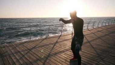 Siyah gömlek ve kırmızı spor ayakkabılar ise eğitim genç erkek boxer sabahın erken saatlerinde deniz kıyısındaki önünde işlemek. Görünmez bir rakiple boks, delme - beyaz kulaklık takan adam