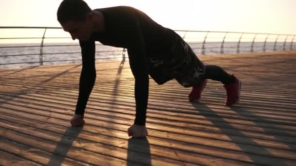 Jovem atleta fazendo flexões em seus punhos ao ar livre na geada de madeira na frente do mar ou do oceano. Fitness e exercício à beira-mar. Esporte, recreação, boxe conceito de estilo de vida — Vídeo de Stock