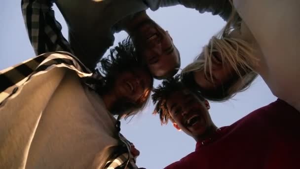 Cuatro jóvenes amigos abrazándose mirando hacia abajo en el suelo posando en un día soleado. Joven con estilo, feliz amistad pasando el rato juntos y sonriendo — Vídeos de Stock