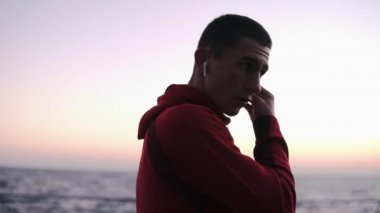 Kulaklıklar üzerinde koyarak ve başlayan genç boksör adam boks yapıyor egzersiz dinle müzik önünde denizin açık havada yaz