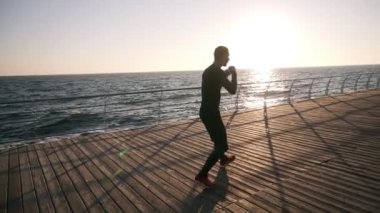 Genç sporcunun siyah gömlek ve kırmızı spor ayakkabılar ise eğitim tam uzunlukta, sabahın erken saatlerinde deniz kıyısındaki önünde işlemek. Görünmez bir rakiple boks, delme siyah giyen adam