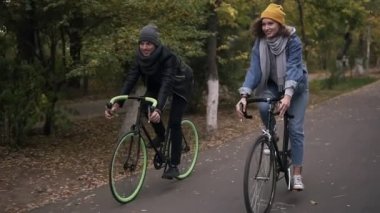 Mutlu, sonbahar parkın içinden trekking bisiklet bisiklet üzerinde Bisiklete binme çift arkadaş veya genç gülümseyen. Erkek ve kadın birlikte bisiklet sürme. Önden görünüm.
