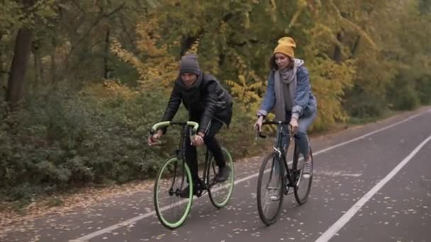 Dos bicicletas. Un par en bicicleta. Ciclismo romántico en el parque de otoño de la ciudad. Hombre y mujer montando bicicletas. Amigos activos de ocio. Movimiento lento — Vídeos de Stock