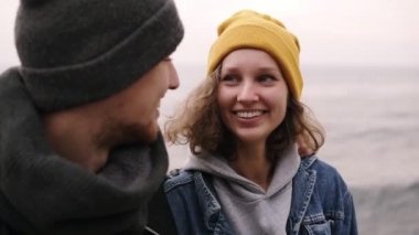 Birlikte ayakta ve deniz kenarında sarılma hipster genç mutlu çiftin yakın çekim. Genç insanlar sıcak giysiler, soğuk havalarda şapka giyiyor. Birbirimizi için gülümseyerek, sarılma
