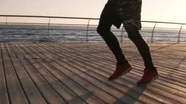 Sağlıklı sporcu giyiyor spor tozluk ve iskele, sahil boyunca güzel sabah gündoğumu sırasında çalışan spor ayakkabı erkek bacakları kesilmiş