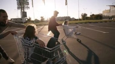Mutlu multirace çiftler gülüyor alışveriş arabaları dans ya da savaş arabası süpermarket Park bölgesinde ile sahiptir. Akşam alacakaranlık