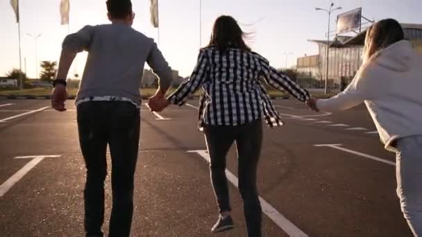 Quatre amis courent dans une zone de stationnement vide à l'extérieur - bonheur amusant, jeunes hommes et jeunes femmes courent au crépuscule et se tiennent la main et sautent librement ensemble. Vue rare — Video